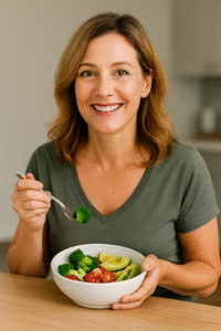 Middle-aged woman smiling while eating a healthy bowl of vegetables during her intermittent fasting window, representing wellness for women over 40.